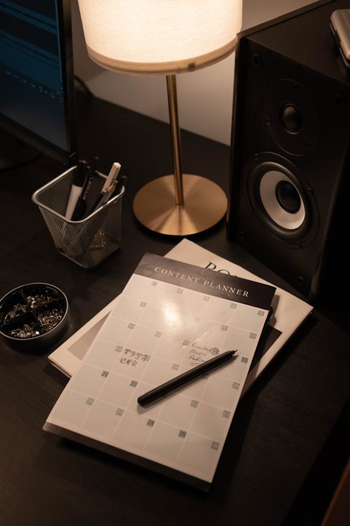 Stylish workspace with a planner, desk lamp, and speaker for a productive vibe.